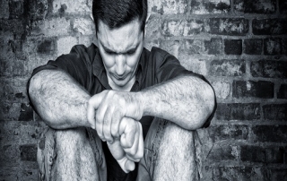 Sad young man sitting on the floor with a bricks background